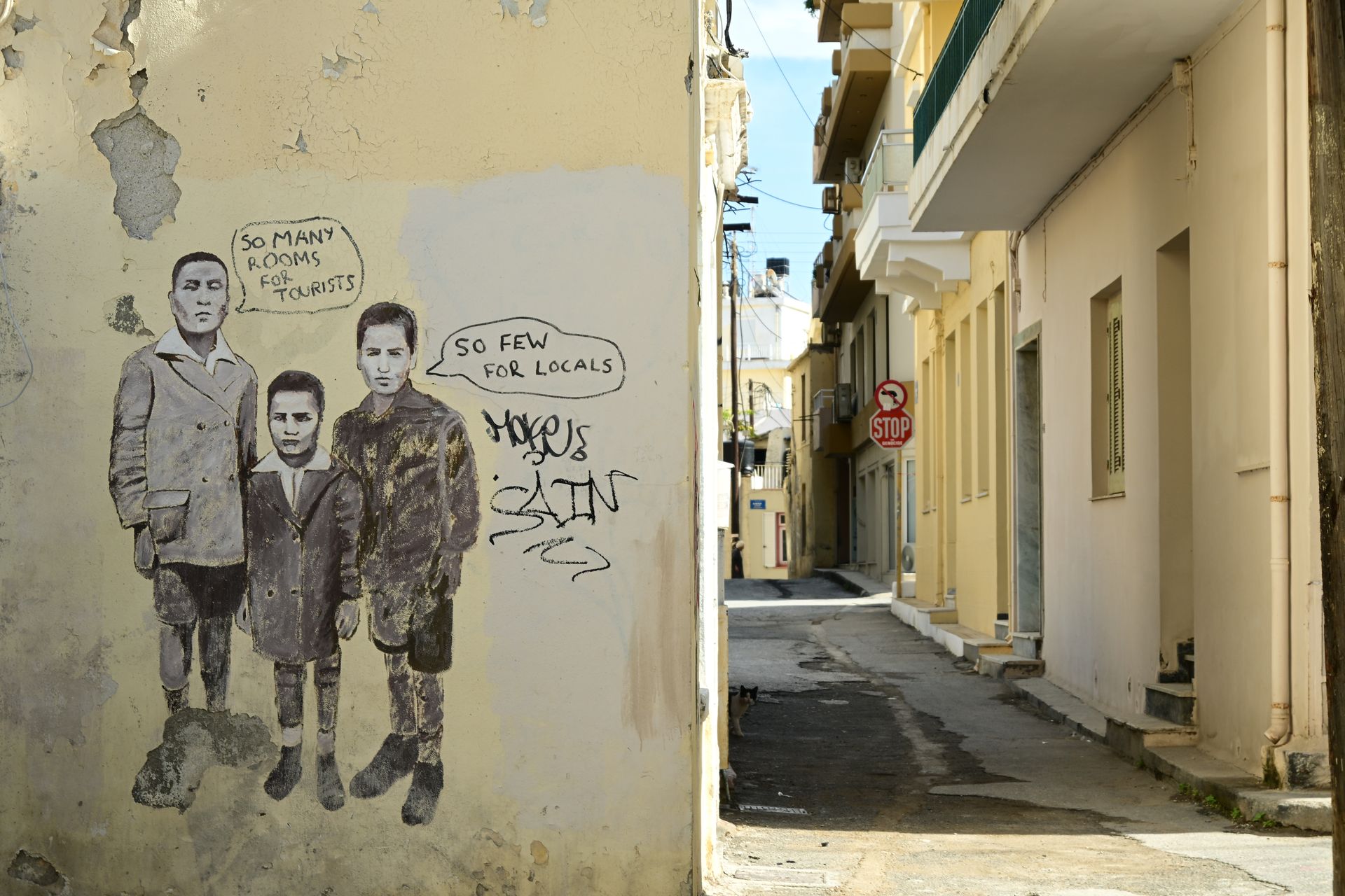 Mural of two figures on a weathered wall beside a narrow street lined with buildings