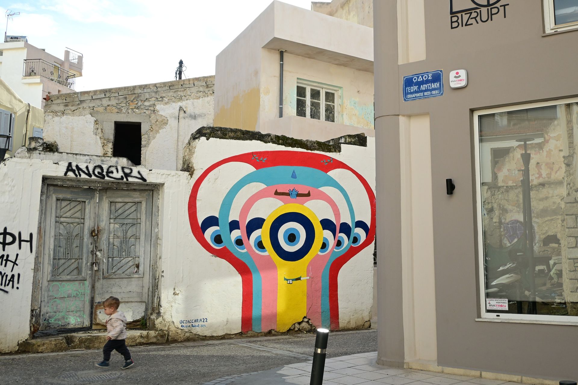 A child walking along a street past a colourful mural beside a renovated entrance