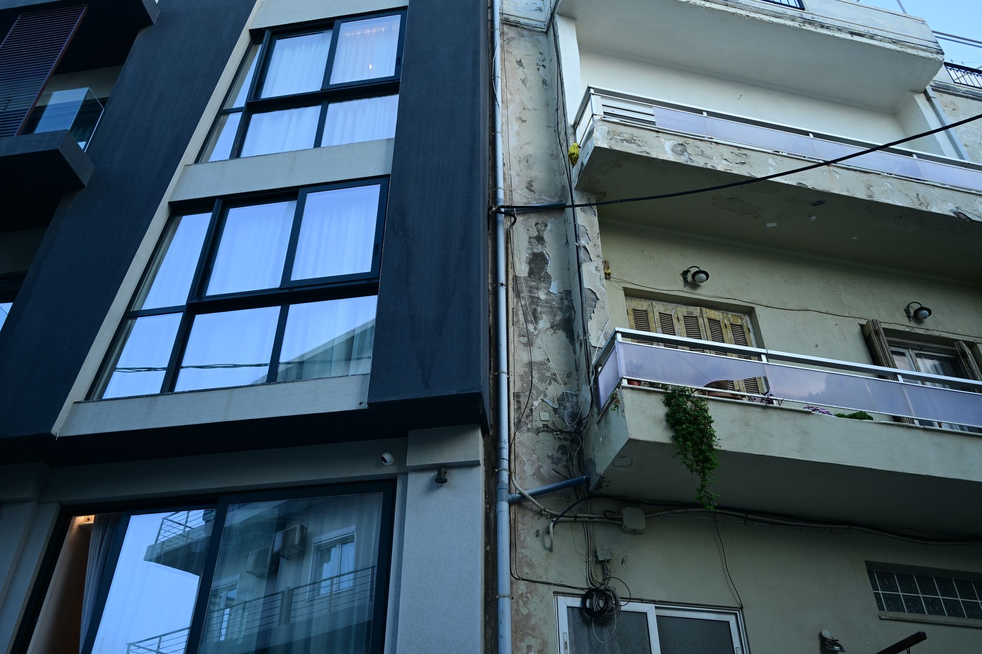 Glazed modern facade beside a weathered building with peeling paint and balconies