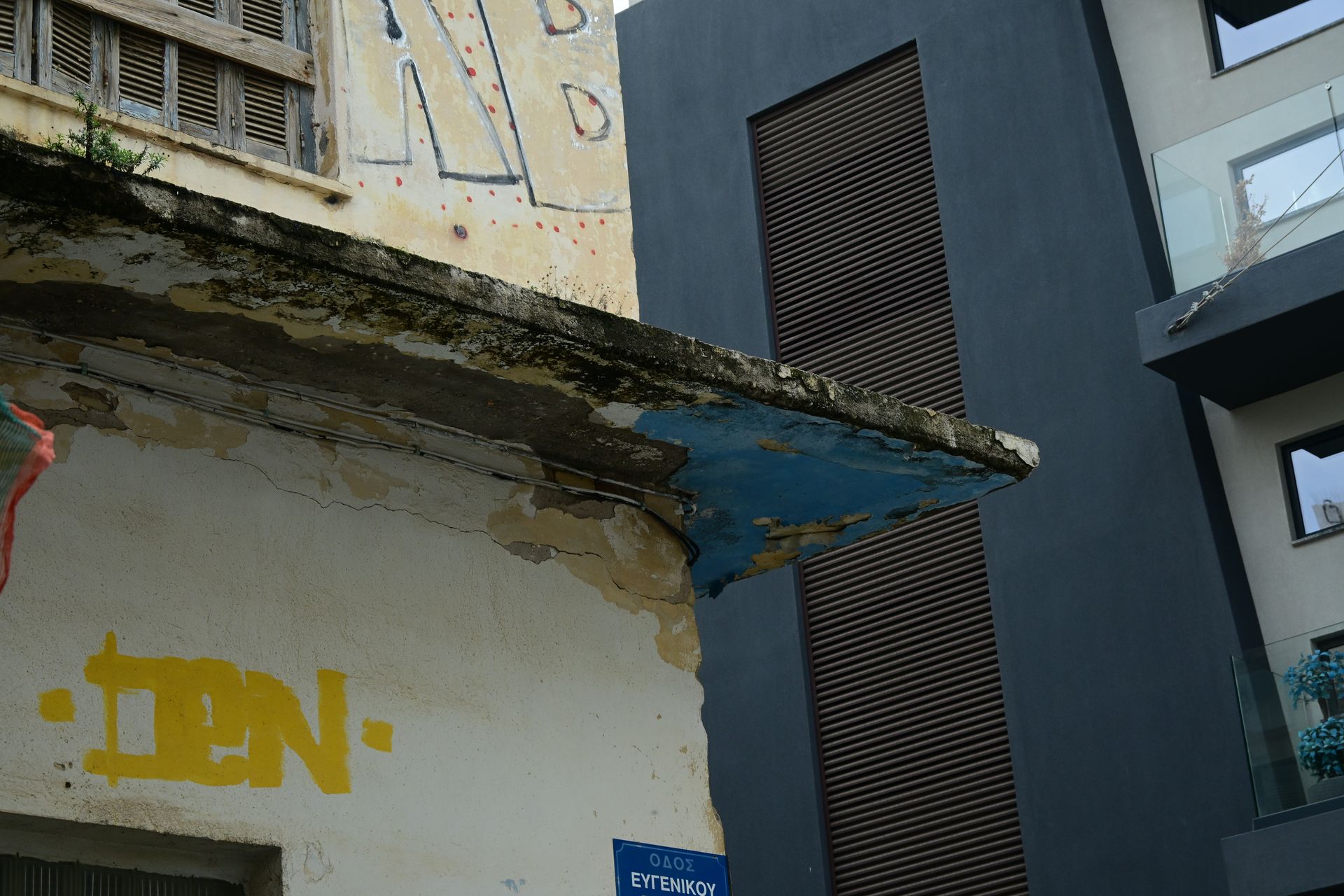Decaying concrete balcony beside a dark facade with a shuttered window