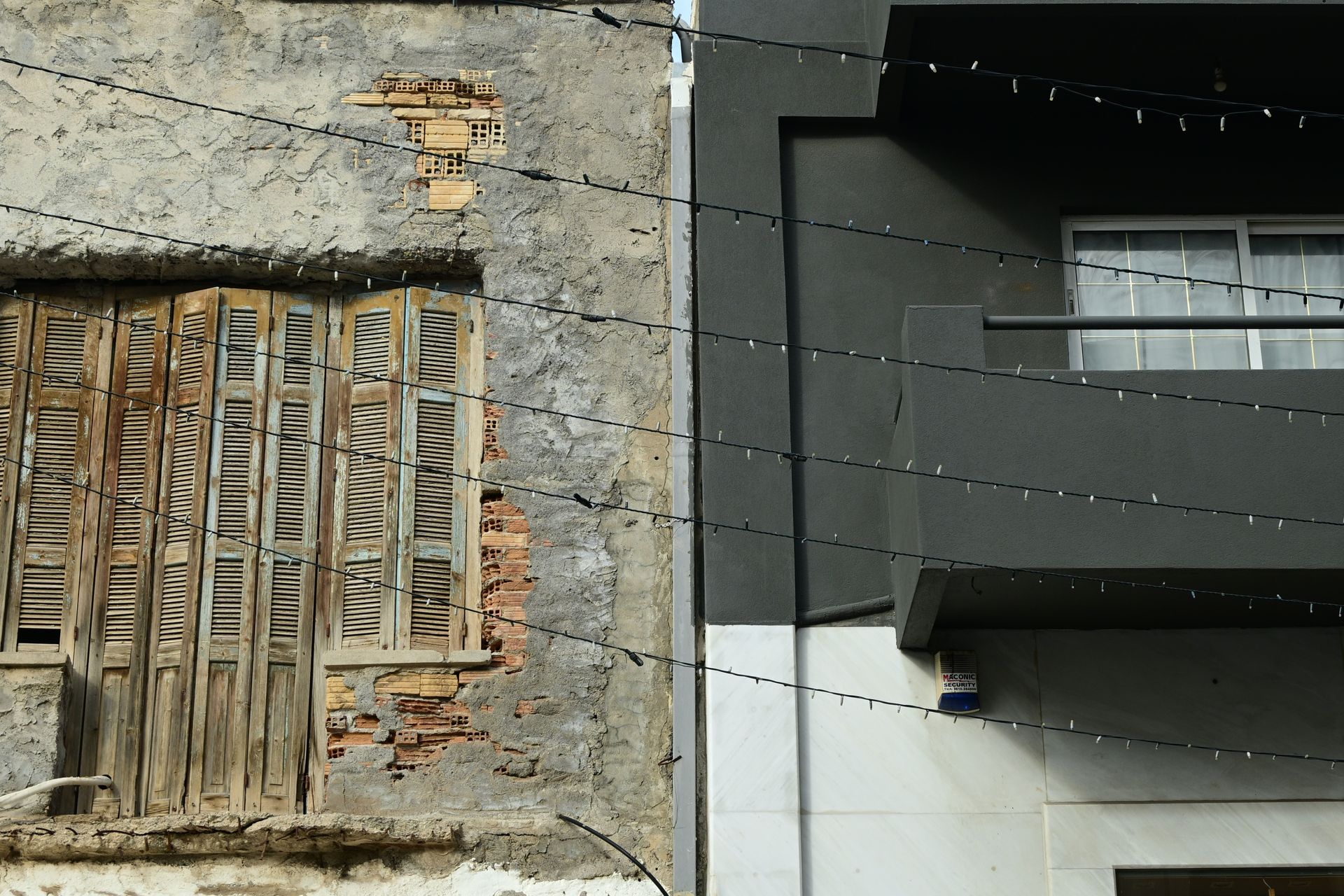 Barred opening in a worn stone facade beside a dark projecting balcony