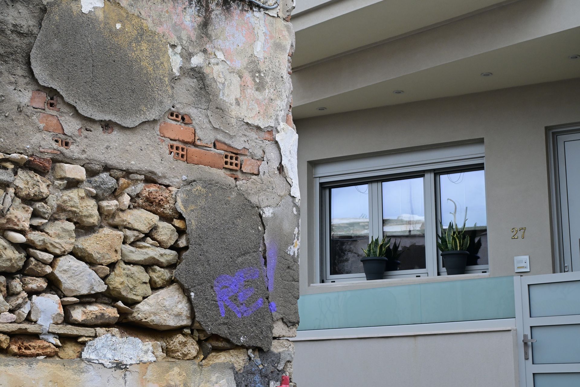 Exposed stone and cracked plaster beside a renovated white window